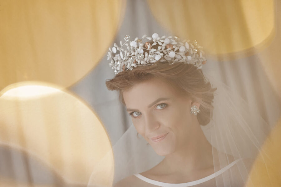 Usmievavá nevesta s ozdobnou čelenkou, elegantnou svadobnou čelenkou a závojom na pozadí jemného žltého bokehu.