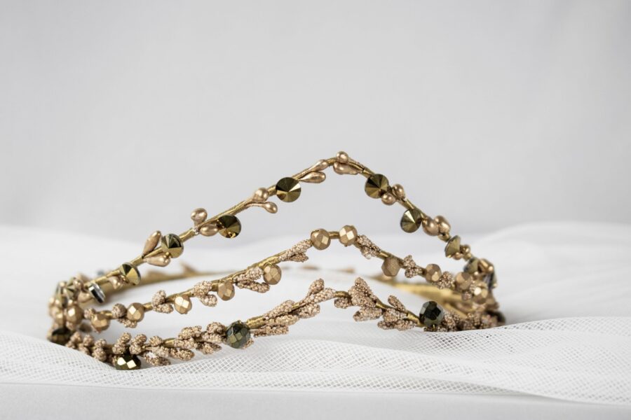 Svadobná čelenka zo zlata, zložito navrhnutá s drobnými korálkami a lístkami, zdobí pozadie z bielej látky a dodáva nádych elegancie každému svadobnému kompletu.