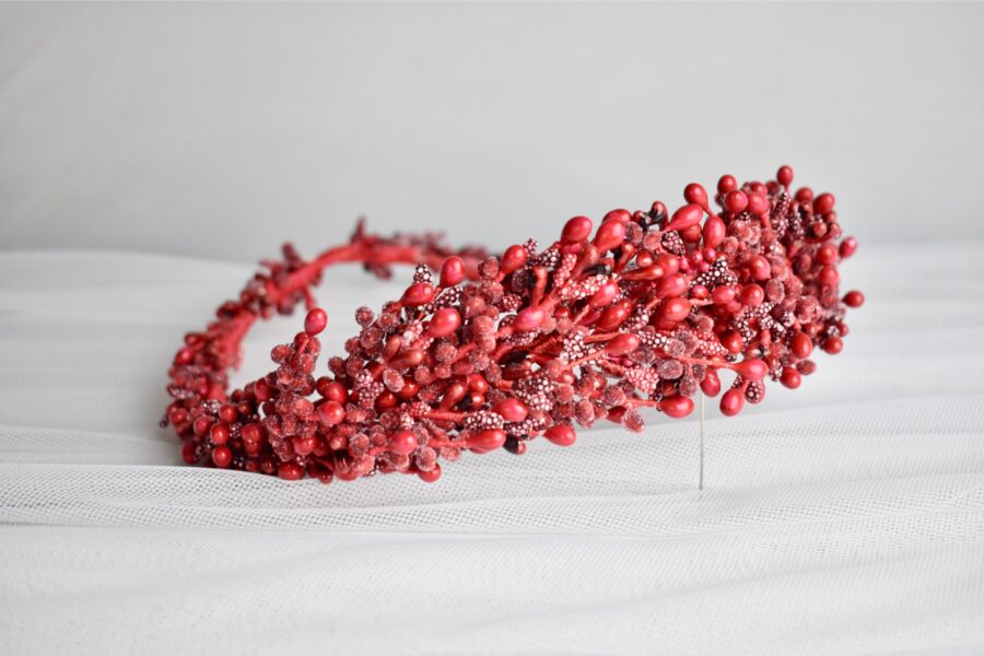 Na bielom štrukturovanom povrchu elegantne spočíva červený bobuľový a korálkový ozdobný veniec, ktorý pripomína svadobnú čelenku.